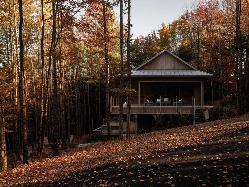 Elevated timber cabin with metal roof and railed deck surrounded by autumn trees and fallen leaves