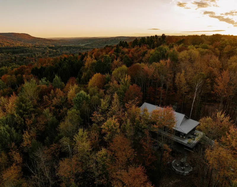 Aerial view of the metal-roofed structure nestled in dense forest at sunset