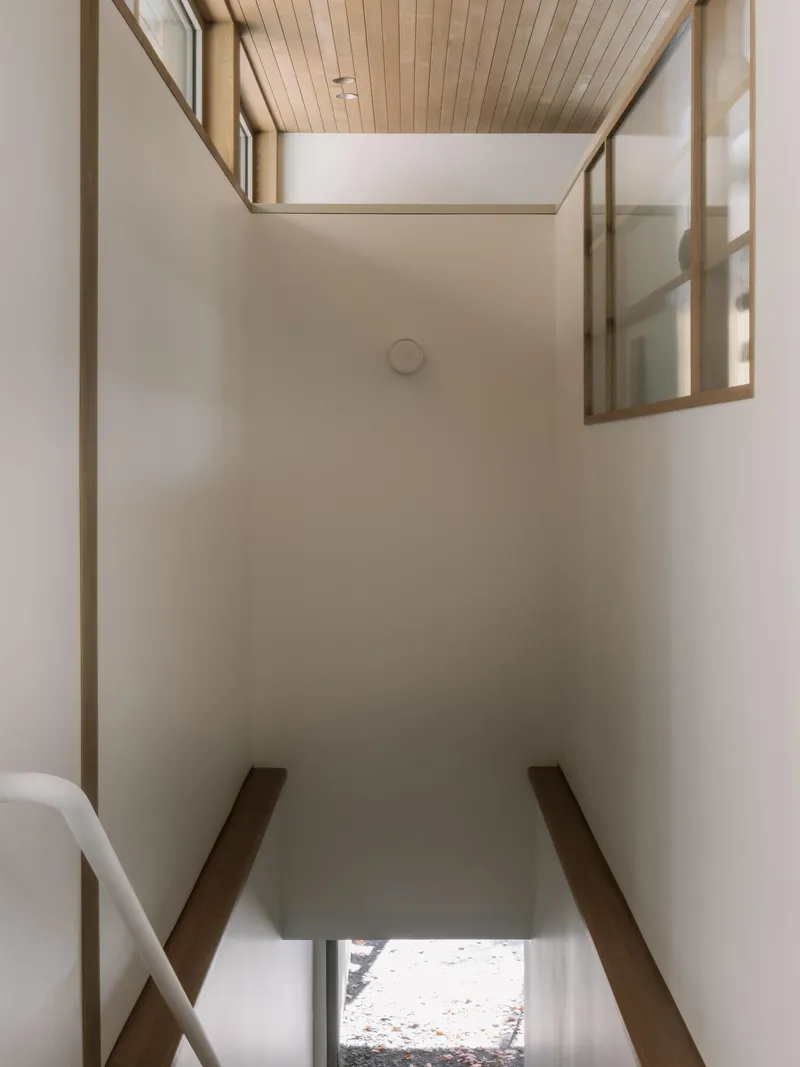 Double-height stairwell with timber-clad ceiling, clerestory glazing and diagonal bracing members flanking white walls