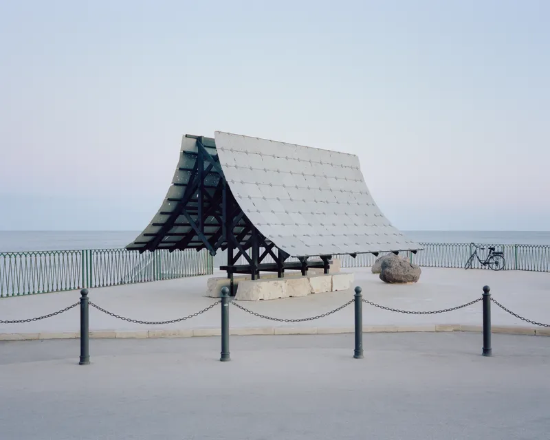 Timber pavilion with white tiled roof and exposed frame on a coastal promenade at dusk