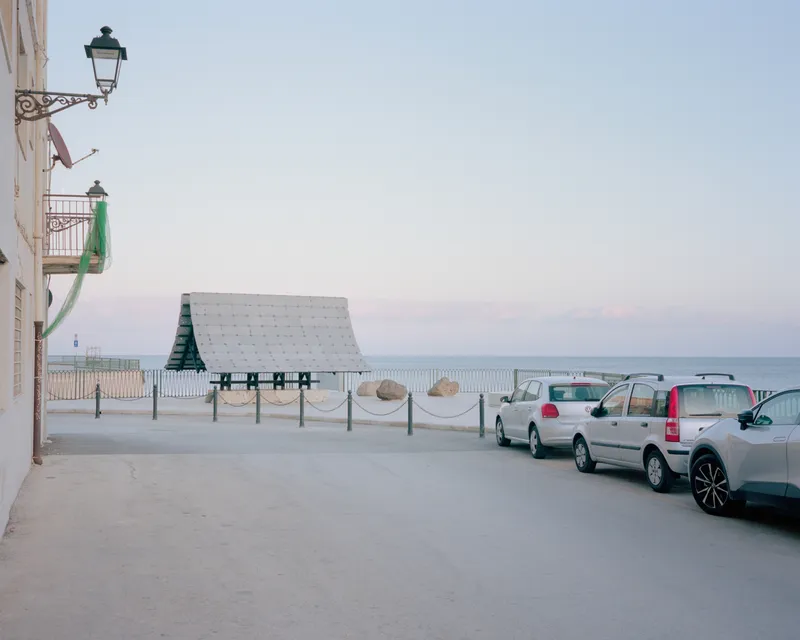 Street view of the pavilion framed by wrought iron balconies and parked vehicles at sunset