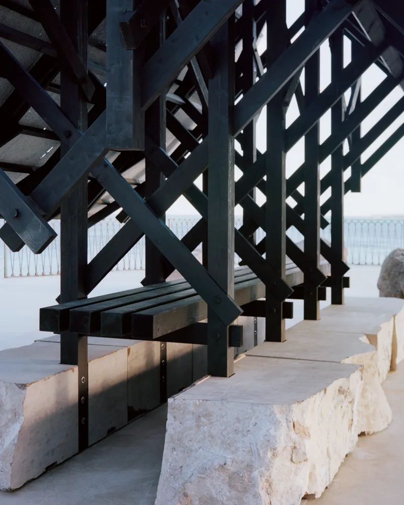 Base detail of the dark timber frame anchored to rough limestone blocks on a concrete terrace