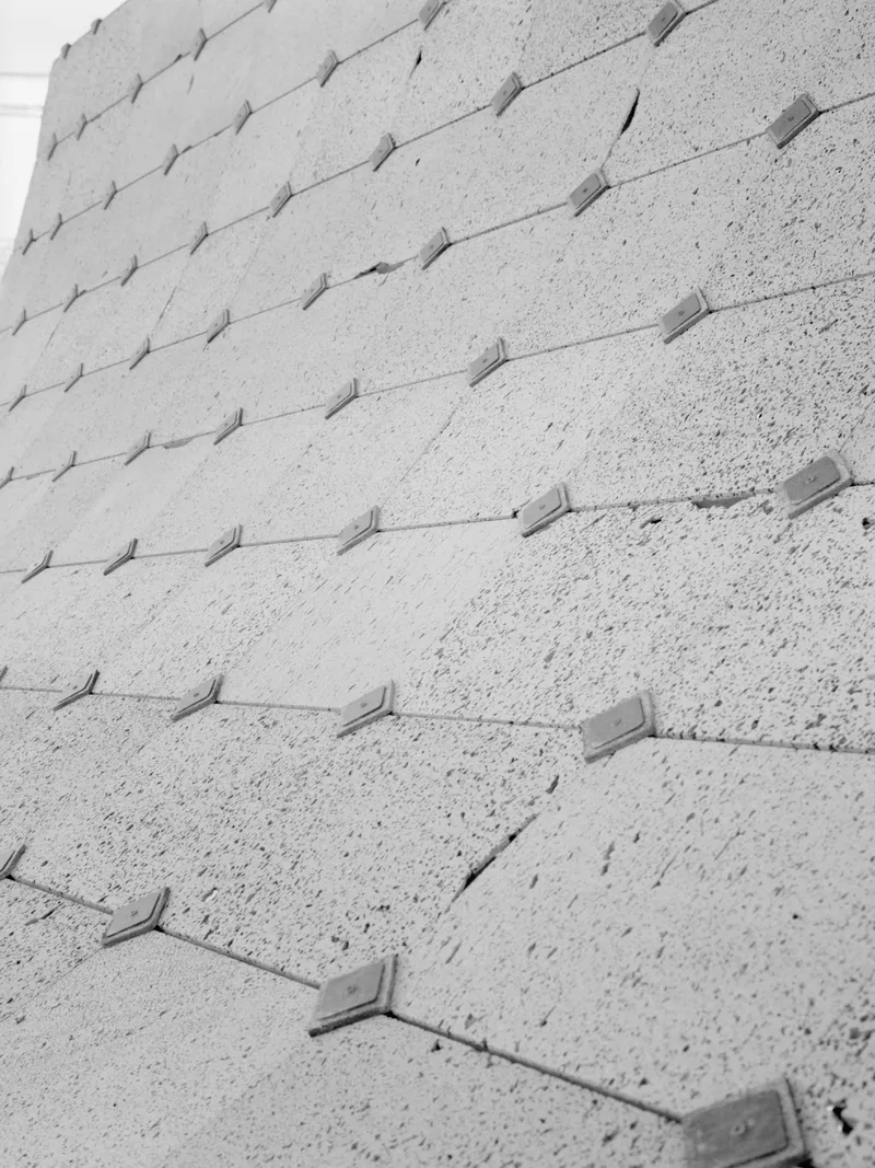 Close-up of textured concrete surface with protruding diamond-shaped metal anchors in diagonal rows
