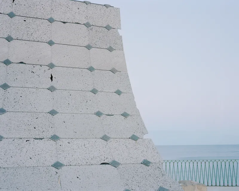 Corner of the tilted concrete wall with metal fixings overlooking a pale blue sea horizon