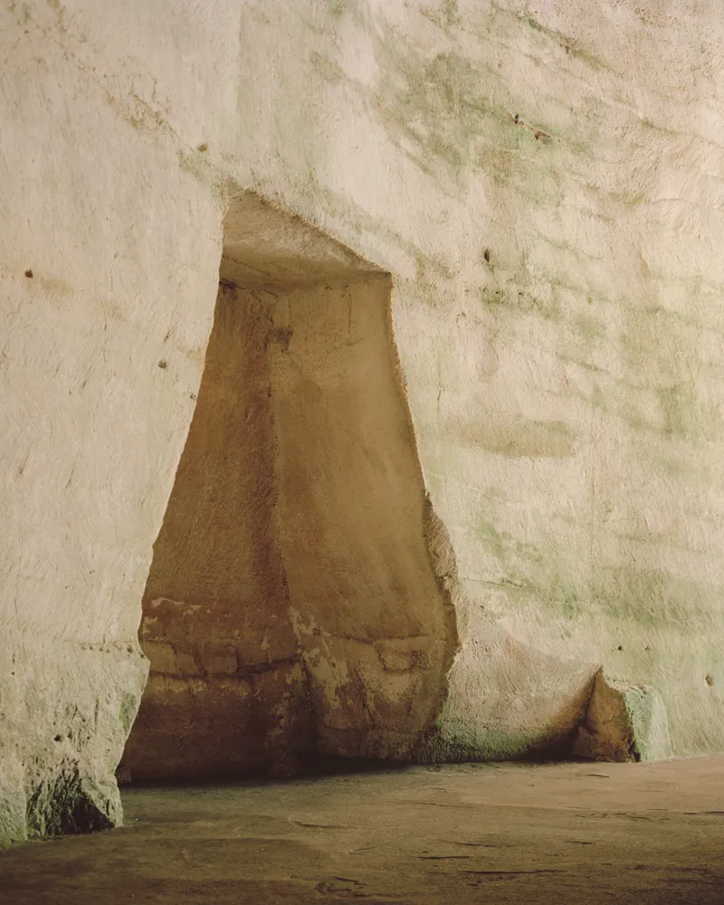 Tapered stone column emerging from whitewashed walls with traces of green moss and weathering
