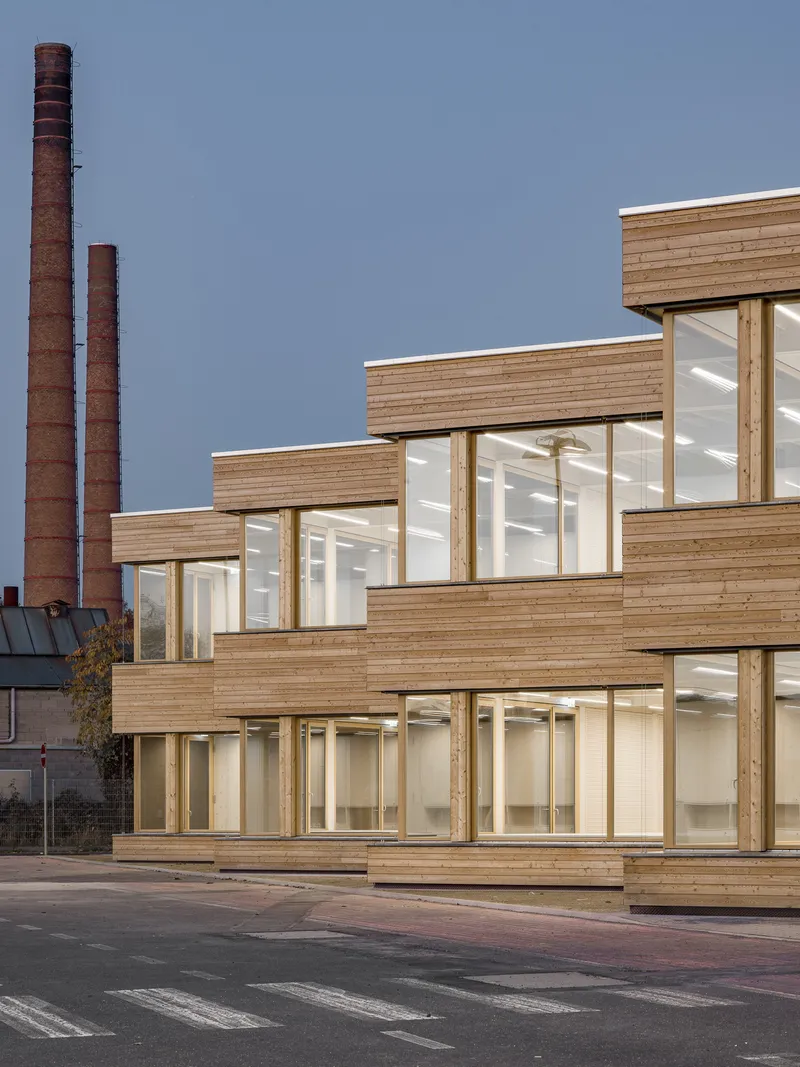 Terraced wood cladding and floor-to-ceiling glazing with industrial chimneys in the background