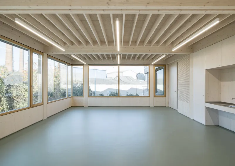 Open workspace with timber beam ceiling and corner windows overlooking nearby trees