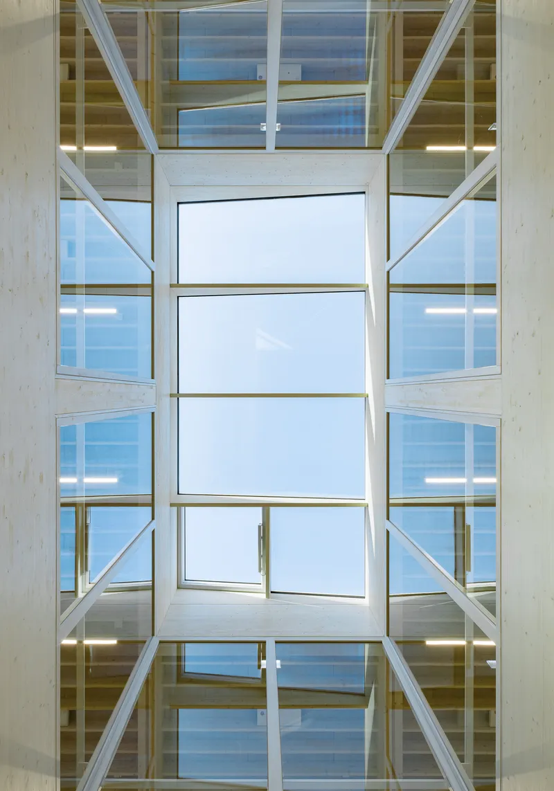Upward view through a multi-story glazed atrium with timber beams and steel bracing