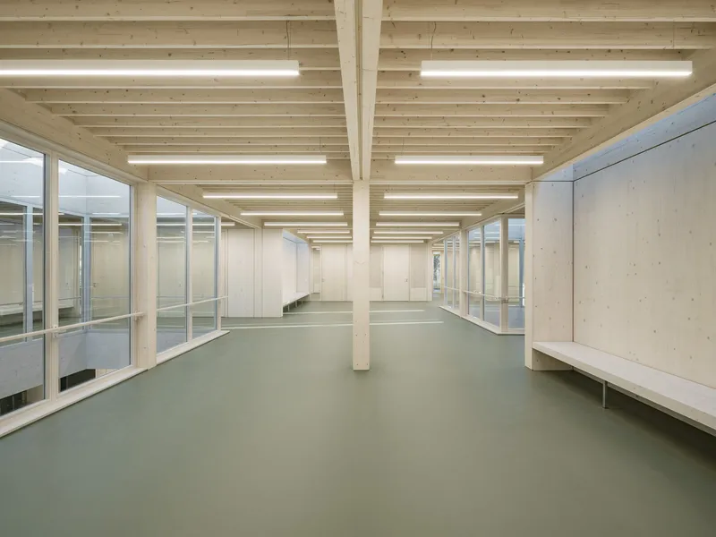 Open floor space with light timber columns and plywood benches under a rhythmic joist ceiling