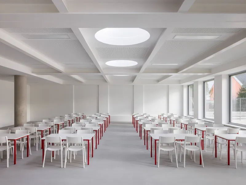 Dining hall with white and red chairs arranged in rows beneath circular ceiling apertures