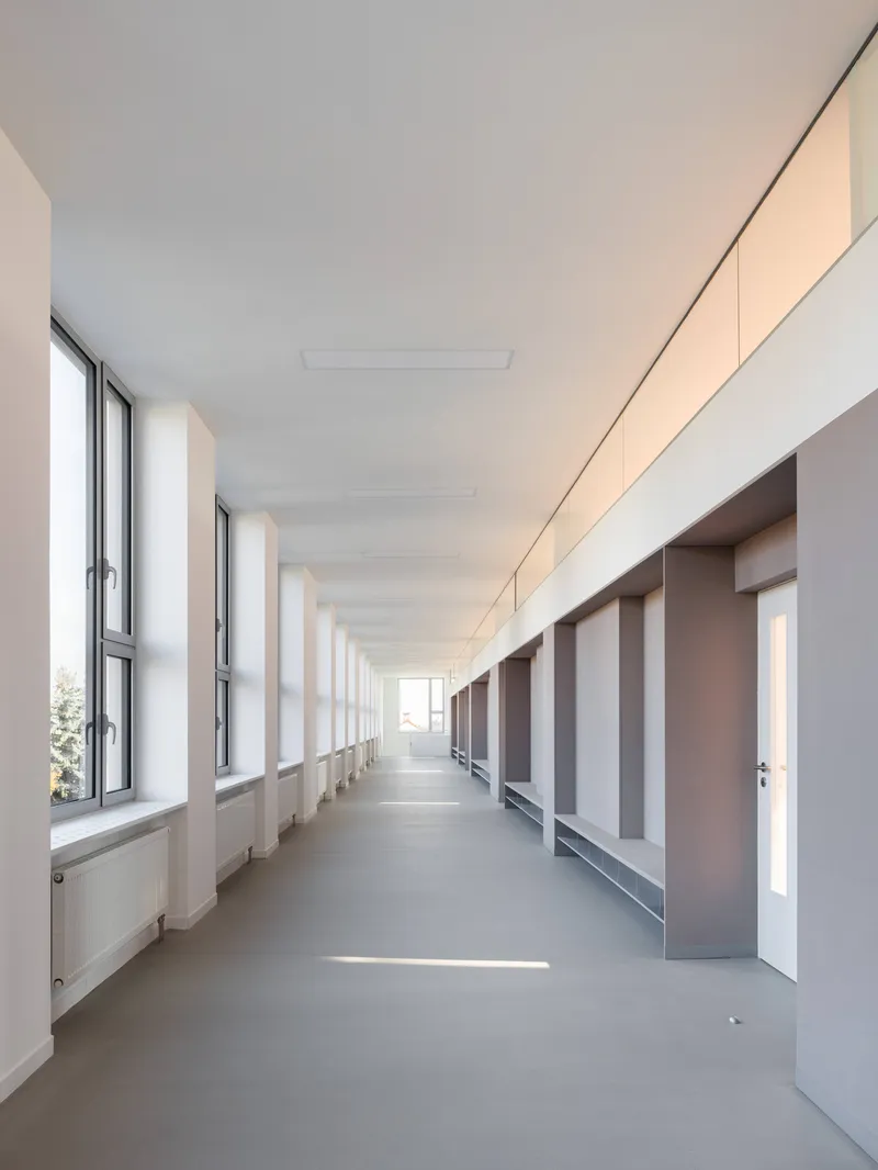 Long corridor with rhythmic window openings on the left and a series of recessed doorways and built-in benches on the right