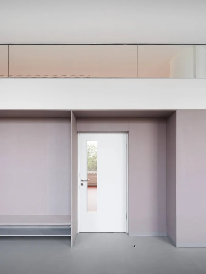 White doorway framed within a deep grey threshold opening beneath a perforated metal ceiling panel and clerestory glazing