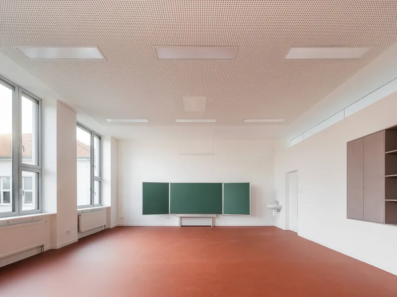 Classroom with green chalkboard panels mounted on white walls and terracotta linoleum flooring beneath a perforated acoustic ceiling