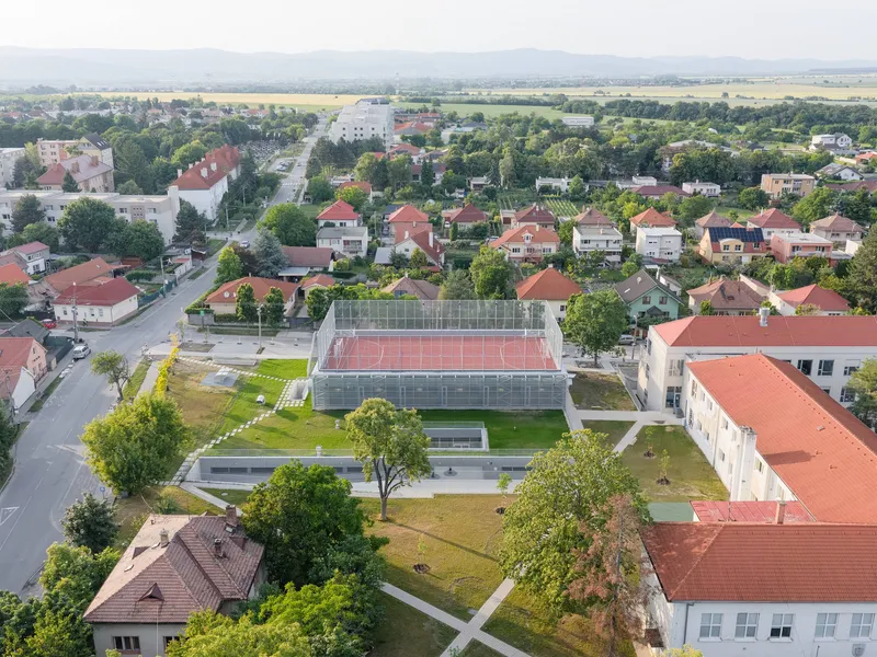 Drone view of the school complex with mesh-wrapped sports hall set among surrounding residential neighborhood