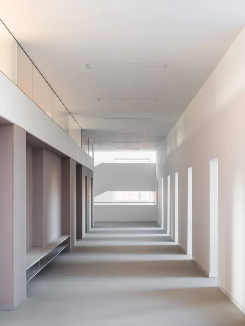 White corridor with rhythmic recessed alcoves along the left wall and daylight filtering from the far end