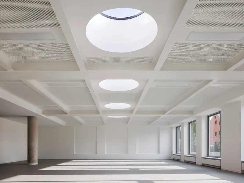 Interior hall with coffered ceiling featuring circular skylights and sunlight casting patterns across the floor
