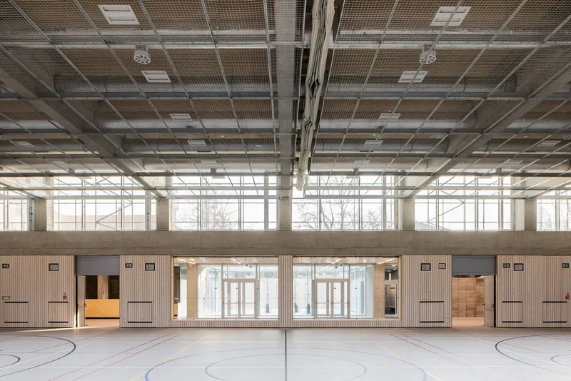 View across the gymnasium showing clerestory windows and timber wall cladding beneath the exposed ceiling structure