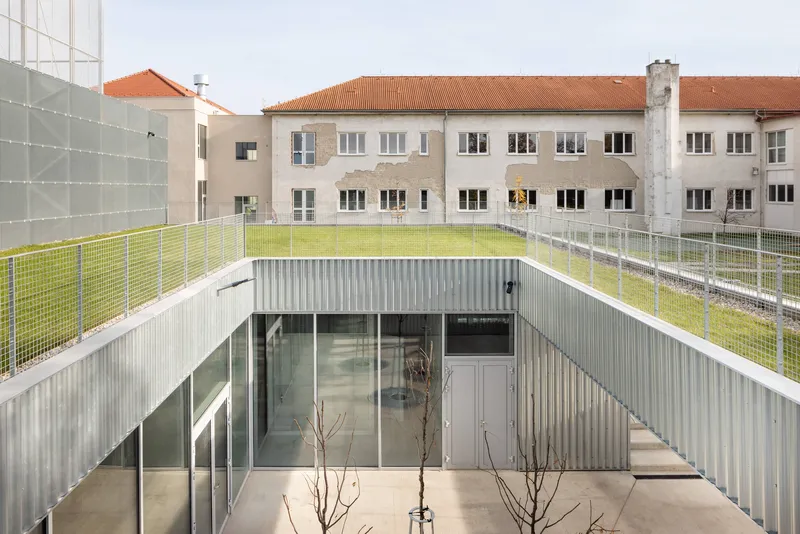 Courtyard view showing recessed volume with corrugated cladding and green roof terrace above existing building
