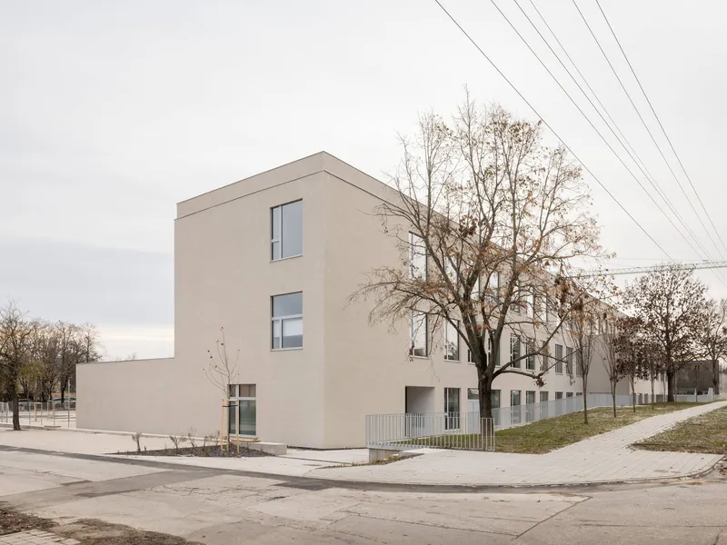 Three-storey rendered plaster block with vertical window strips under bare winter trees