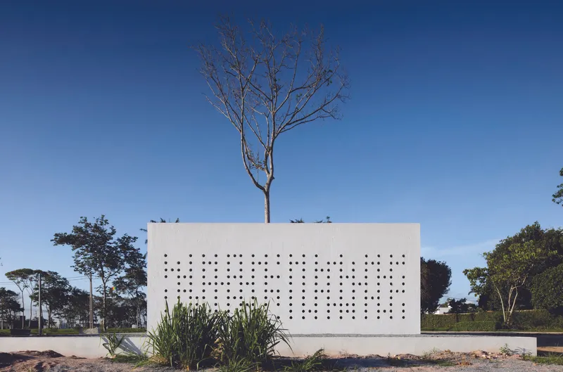 Perforated white facade with planted bed below and bare tree rising through the roof