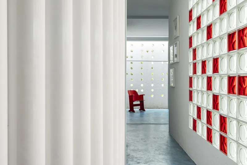 Corridor with white fabric curtain and red and clear glass block wall with a red chair visible beyond