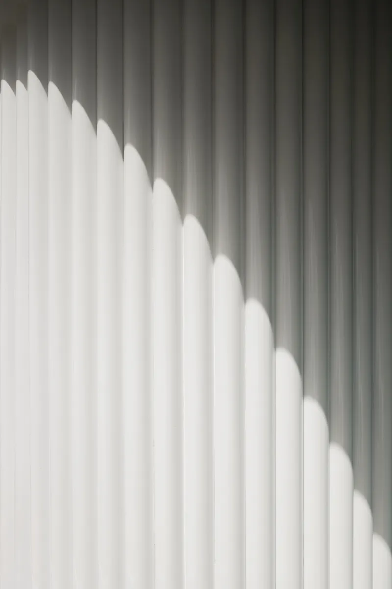Diagonal shadow pattern cast across white vertical slat wall in natural daylight