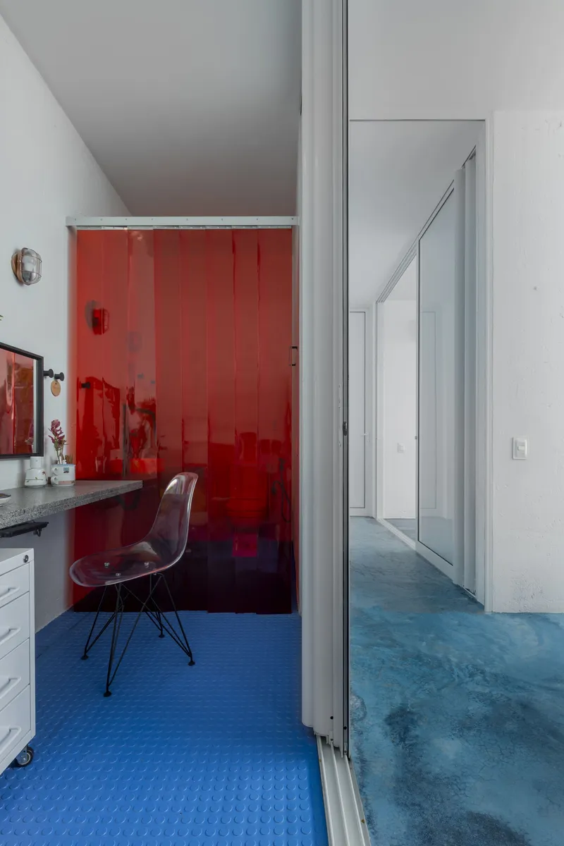 Blue rubber floor meets red translucent glass wall enclosing a dressing area with vanity and chair