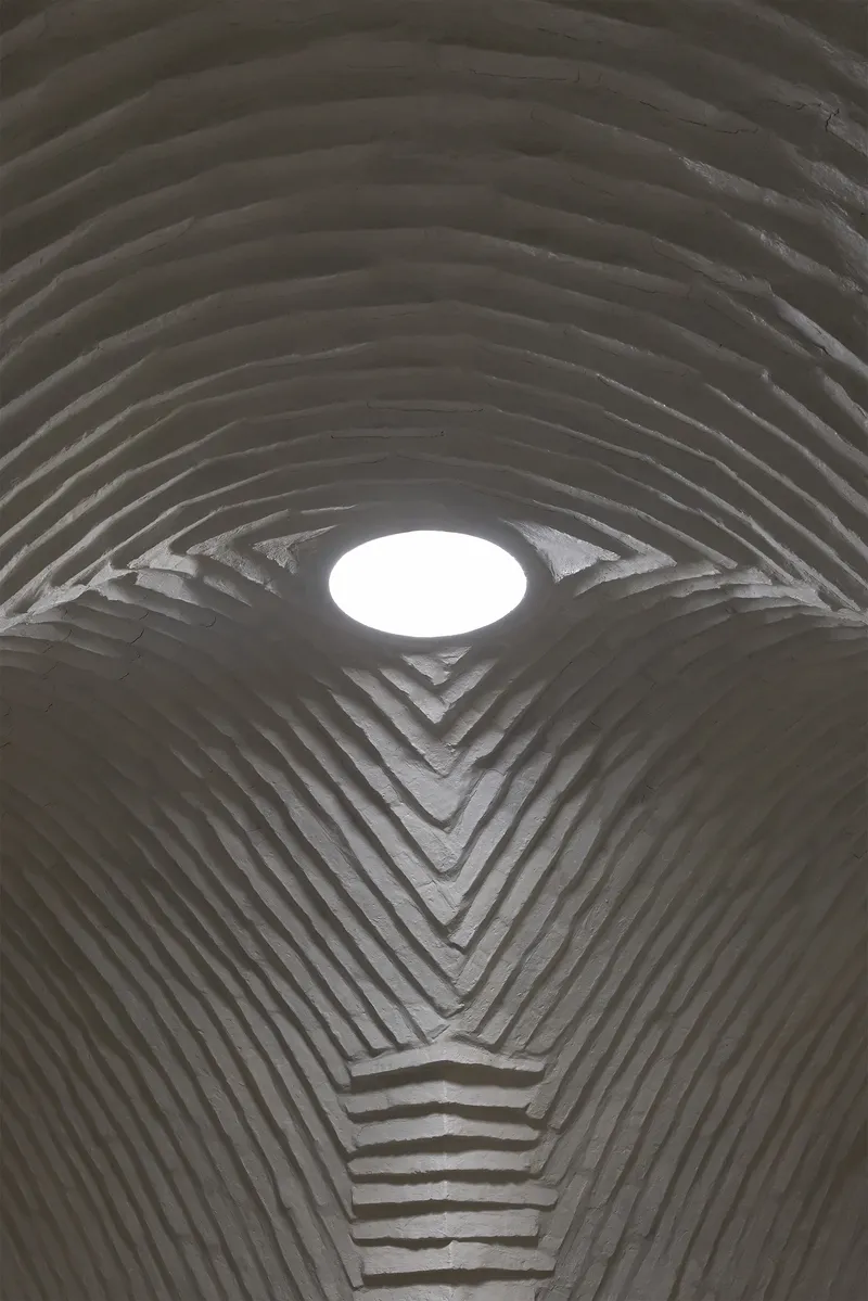 Looking up at circular skylight set into ribbed concrete vault with chevron junction