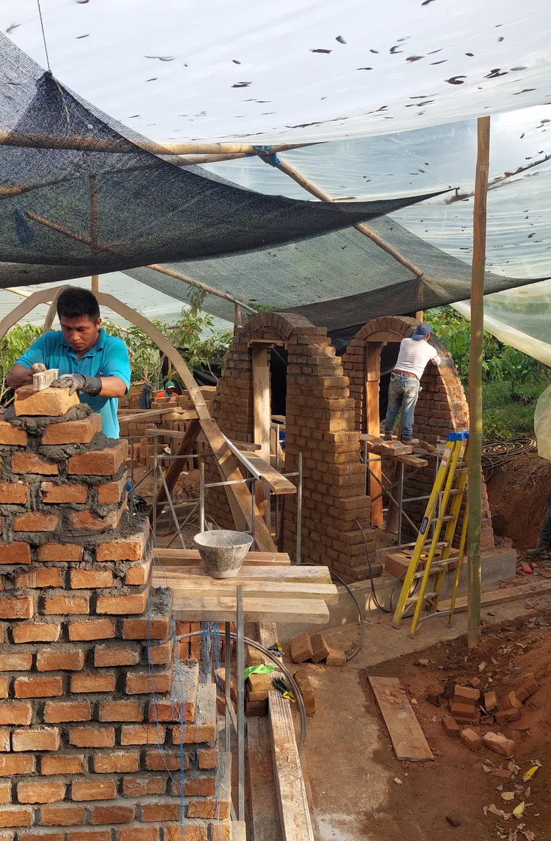 Construction site with workers building curved brick vaults beneath a temporary fabric canopy