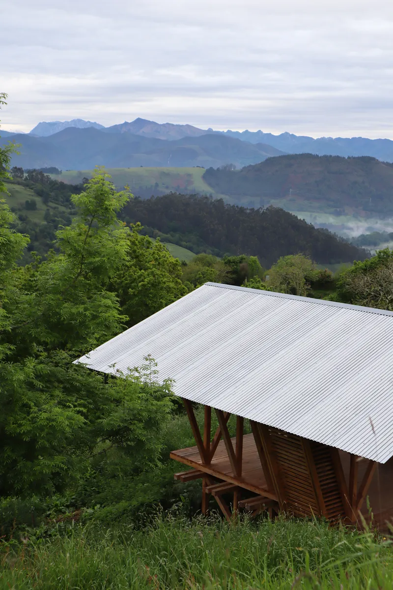 Open-sided structure with corrugated roof and timber frame overlooking layered mountain ridges with morning mist