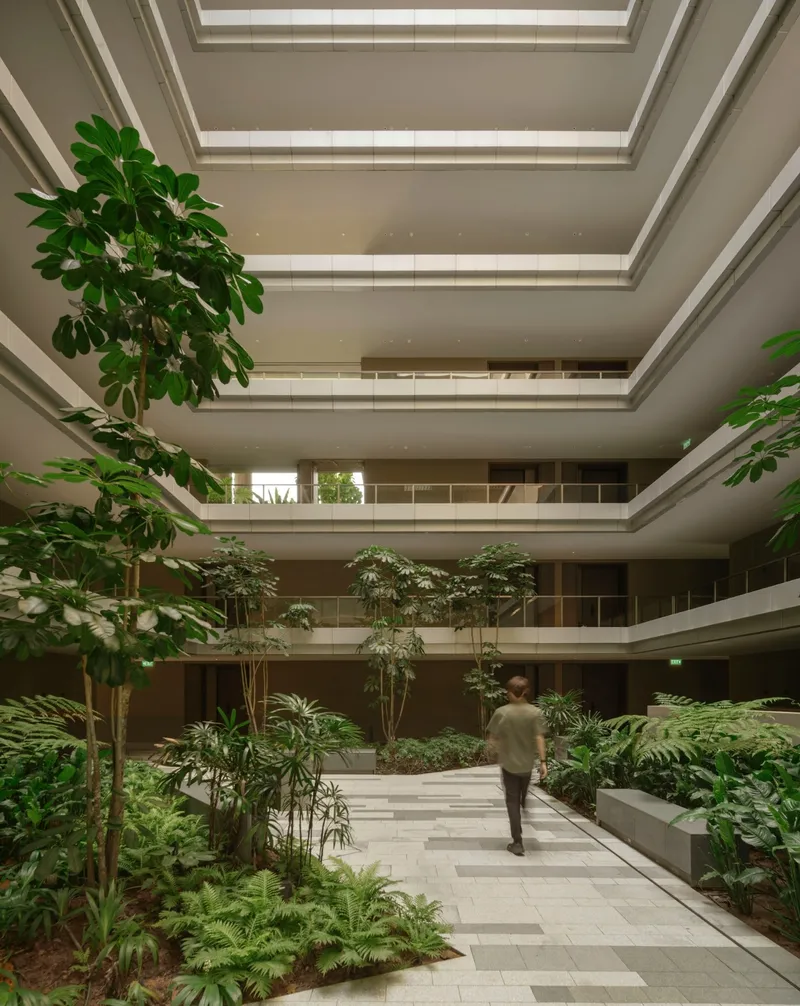 Interior courtyard atrium with planted beds, walking path, trees and skylights above as a figure passes through