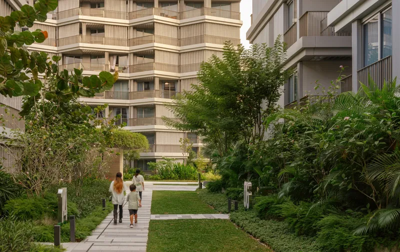 Pathway through a planted courtyard with two residents walking past residential towers under soft daylight