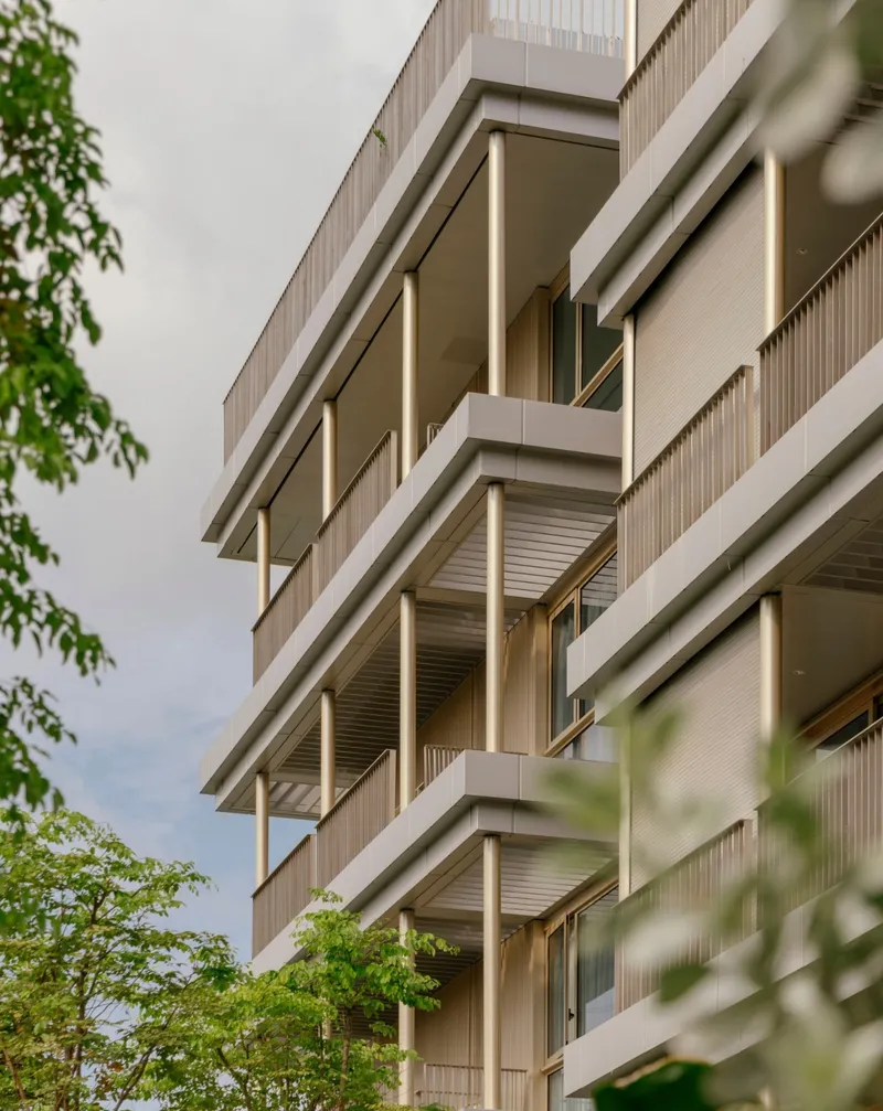 Corner view of staggered balconies with integrated lighting and timber cladding framed by foliage at dusk