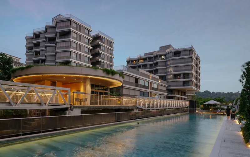 Long pool with pavilion and residential blocks illuminated at dusk beneath a clouded sky