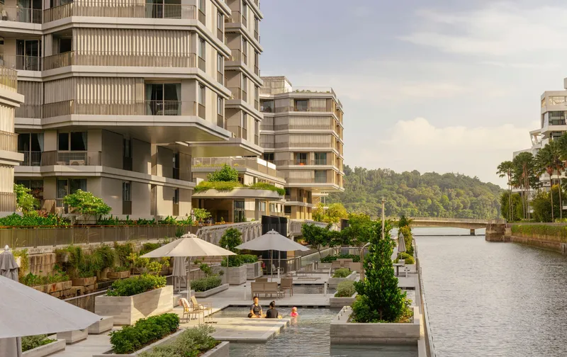 Terraced waterfront plaza with planters, umbrellas and seating alongside residential blocks under cloudy skies