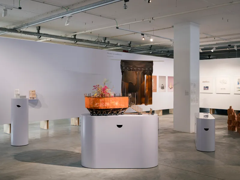 Exhibition space with sculptural installation on white plinth beneath exposed ceiling ducts and track lights
