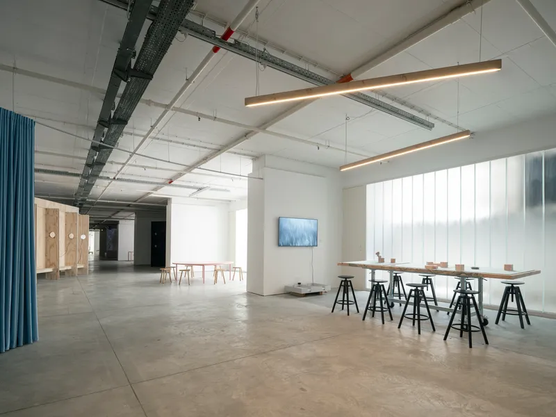 Open gallery space with work table on trestles and vertical white panel wall under linear pendant lights