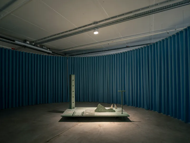 Enclosed gallery alcove with deep blue curtain walls surrounding a centered sculptural installation on platform