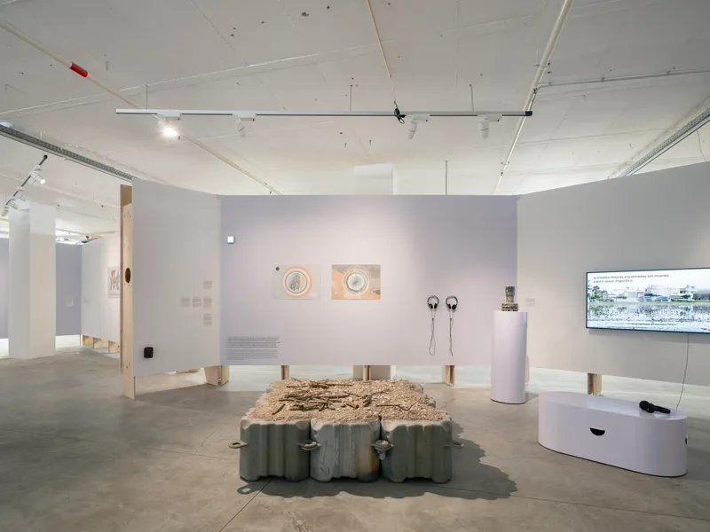 Gallery interior with white walls displaying artworks and a central table with textured surface under track lighting