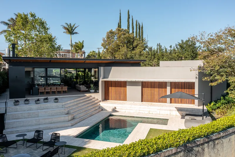 Rear courtyard with travertine pool deck and timber-clad volume framed by mature trees