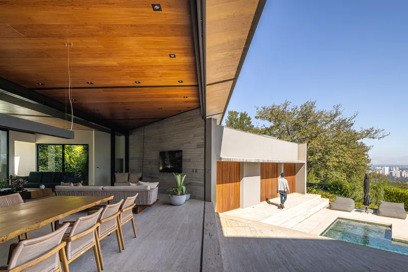 Covered outdoor dining terrace with wood ceiling opening to poolside courtyard in afternoon light