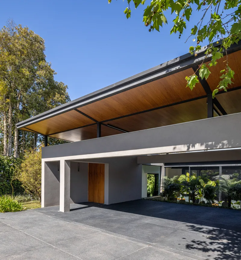 Entry canopy with exposed timber soffit and steel beams under dappled tree shade