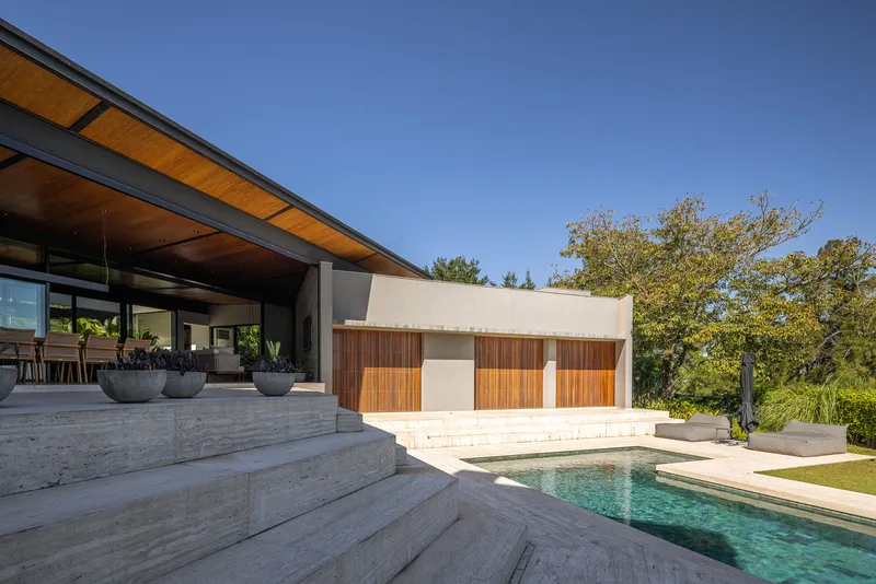 Pool terrace with board-formed concrete steps leading to pavilion and timber-clad structure beyond