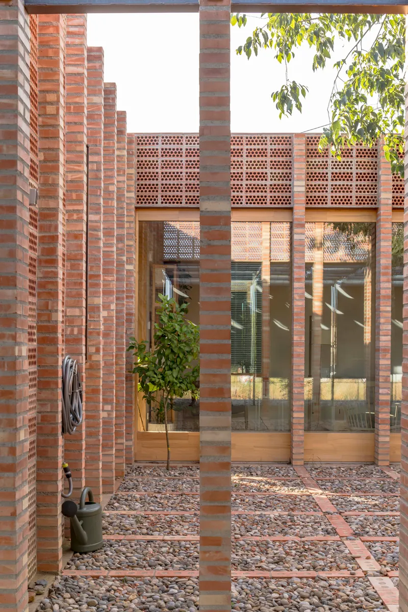 View through perforated brick columns into a courtyard with gravel and glazed doors