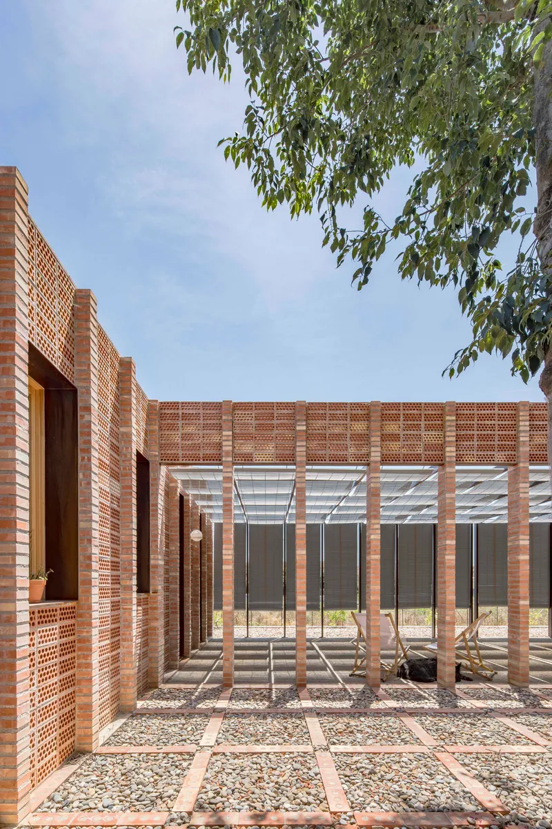 Courtyard with brick pergola columns and gravel grid pathways beneath tree branches overhead