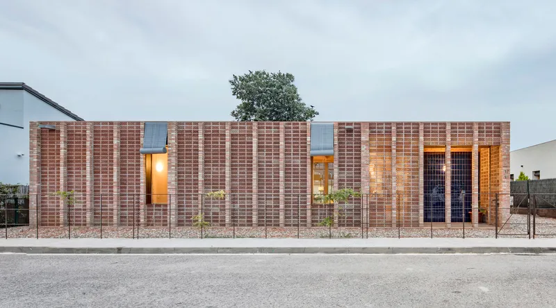 Street facade with layered brick walls and illuminated window openings at dusk