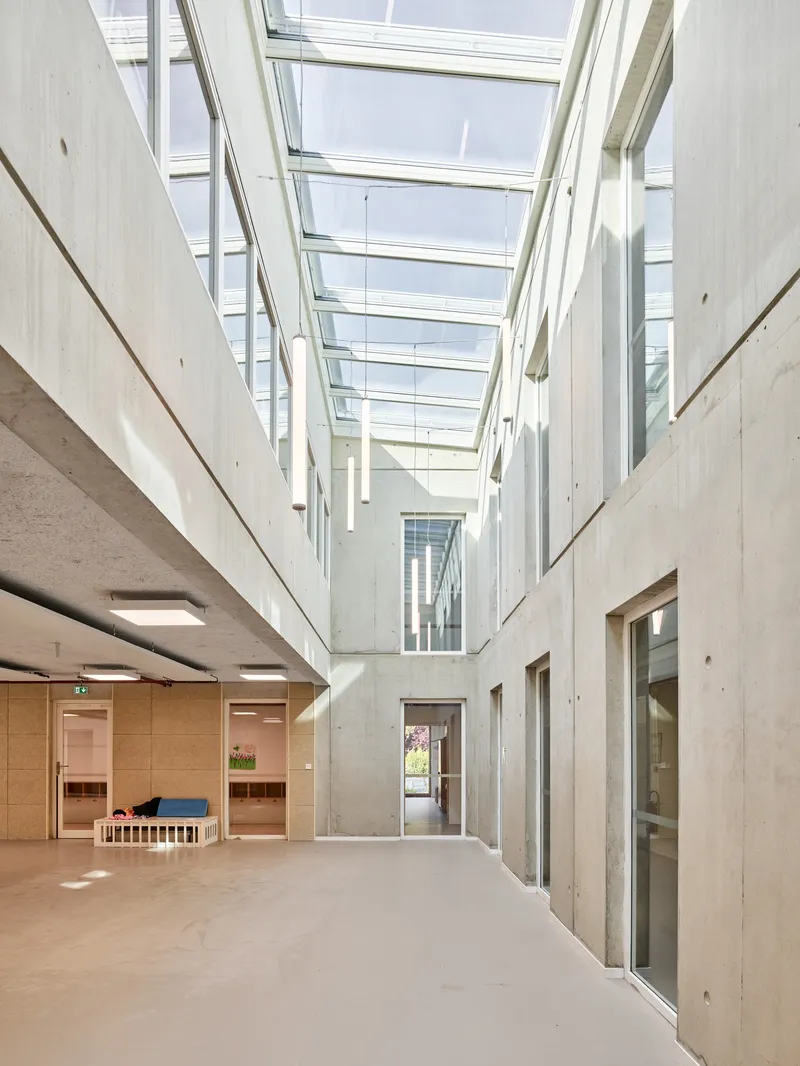 Skylit corridor with exposed concrete walls and timber-clad doorways beneath the glazed ceiling