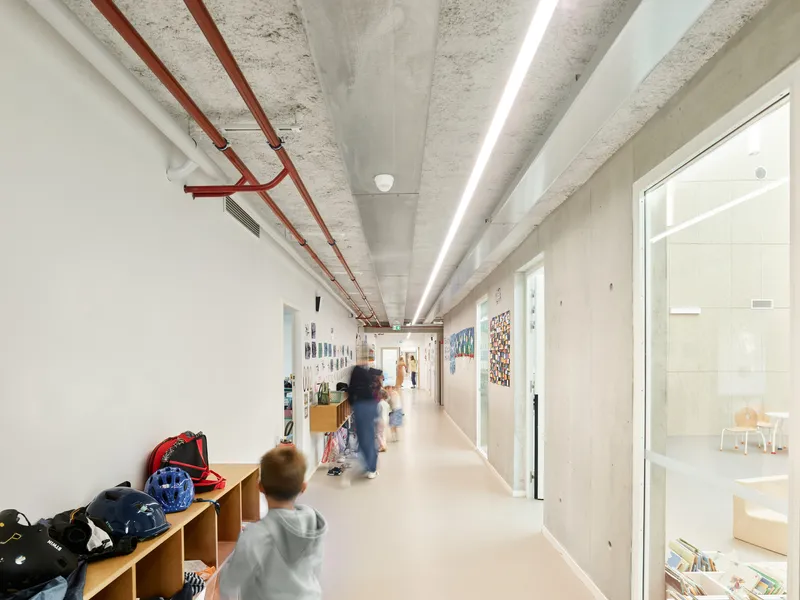 Hallway with exposed red conduit along the concrete ceiling as children walk past storage cubbies