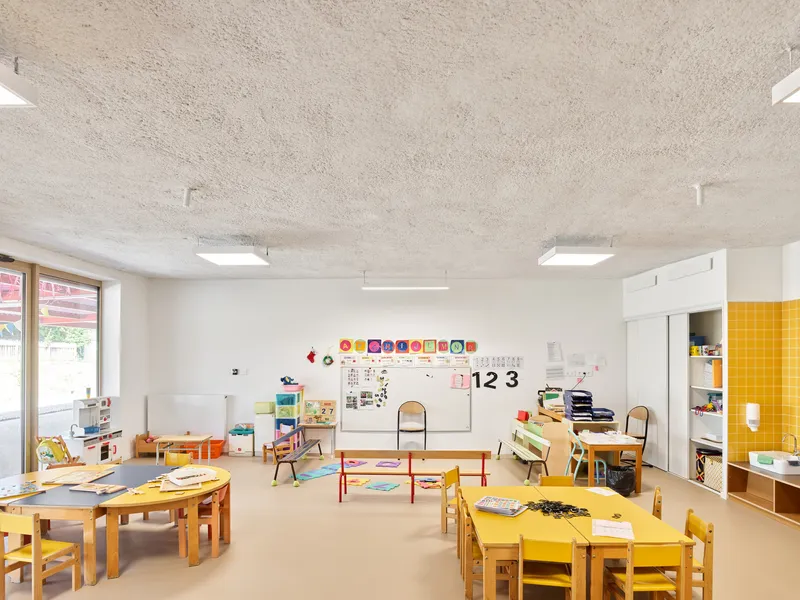 Classroom with yellow tile partition, round timber tables and exposed concrete ceiling above white walls