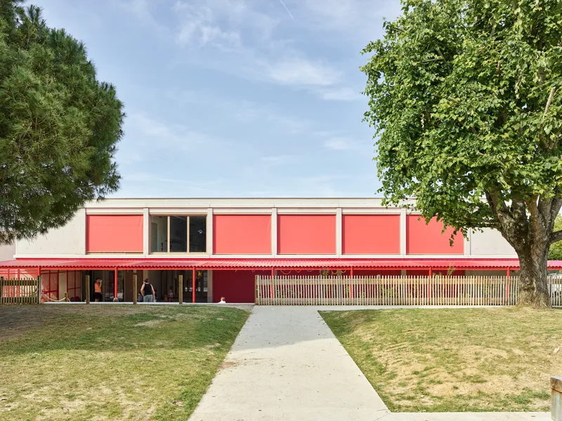 Two-storey facade with coral panel infill and horizontal timber screening framed by mature trees